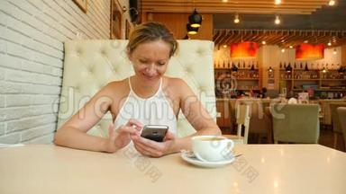 一个金发女人正坐在一个炎热的夏天的咖啡馆里，微笑着在手机上输入短信。 4k.慢